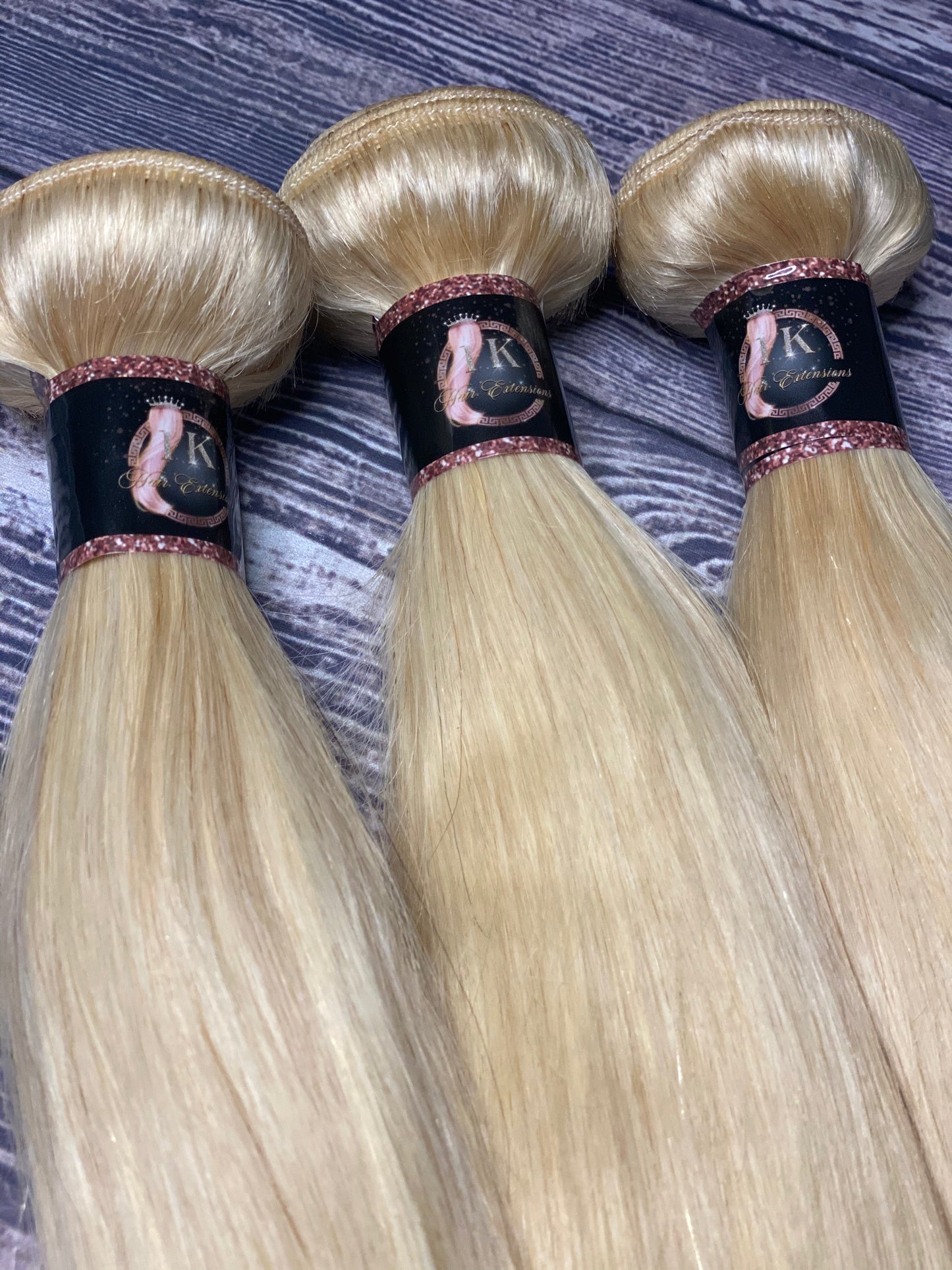 Three bundles of blonde hair extensions on a textured surface